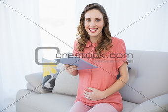 Cheerful pregnant woman holding her tablet sitting on a couch