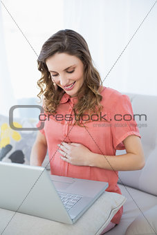 Peaceful pregnant woman working with her laptop sitting on a couch in the living room