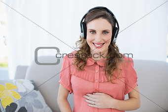 Happy beautiful pregnant woman relaxing in the living room listening to music