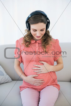 Gorgeous pregnant woman listening to music sitting in the living room