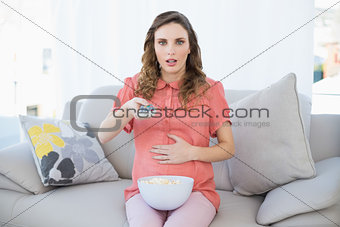 Astonished pregnant woman sitting in living room watching television
