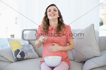 Amused pregnant woman watching television while sitting on couch in the living room