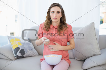 Young pregnant woman watching television sitting on couch