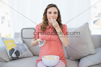 Cute pregnant woman eating popcorn while watching television