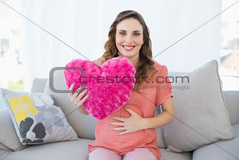 Content pregnant woman holding a pillow sitting on couch in living room