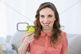 Smiling pregnant woman presenting green apple sitting in living room