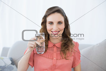 Pretty pregnant woman showing glass of water sitting on couch