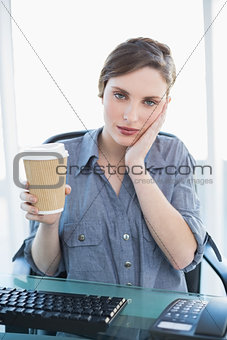 Tired casual businesswoman holding a disposable cup while sitting at her desk
