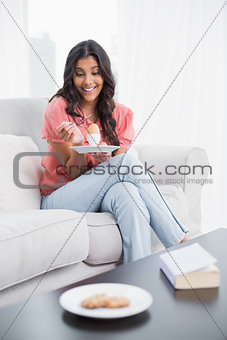 Happy cute brunette sitting on couch holding hard boiled egg