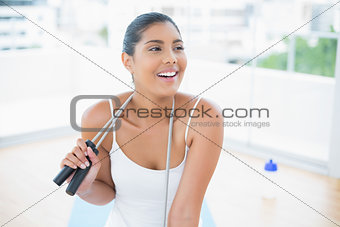 Cheerful toned brunette sitting on floor with skipping rope
