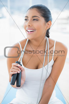 Laughing toned brunette sitting on floor with skipping rope