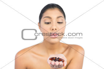 Unsmiling nude brunette holding tablets in open hand
