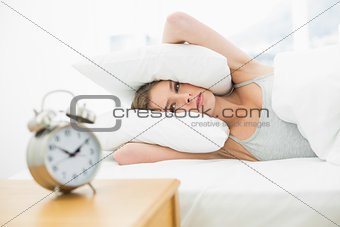 Tired young woman lying in her bed covering her ears with pillow