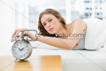 Annoyed beautiful woman turning off the alarm clock while lying in her bed