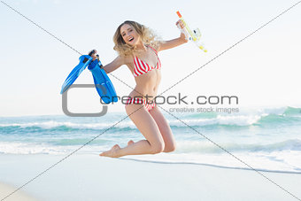 Happy woman jumping while holding flippers and a snorkel and diving goggles