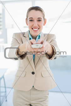 Attractive businesswoman holding a remote smiling cheerfully at camera