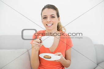Attractive brunette woman holding a cup smiling cheerfully at camera