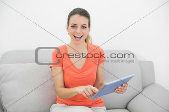Beautiful casual woman using her tablet looking cheerfully at camera