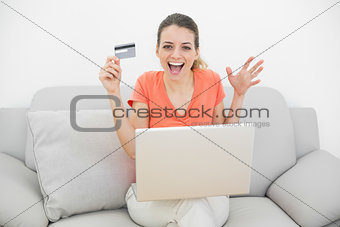 Happy casual woman showing her credit card using her notebook