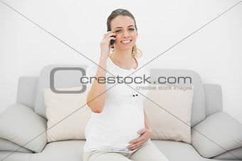 Gorgeous pregnant woman phoning with her smartphone smiling at camera