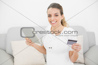 Attractive pregnant woman showing cheerfully her credit card and tablet