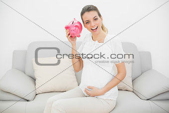 Happy pregnant woman shaking a pink piggy bank