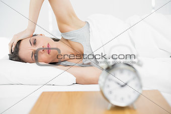 Suffering young woman lying on her bed touching her head