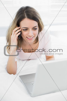 Cheerful brunette woman phoning with smartphone lying on her bed