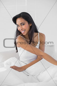 Cute woman smiling cheerfully at camera sitting on her bed