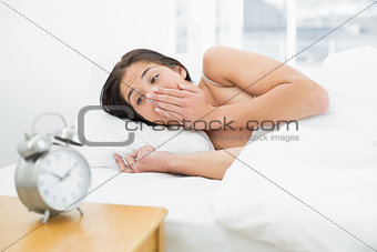 Shocked woman in bed looking at alarm clock