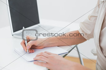 Midsection of a businesswoman writing notes by laptop