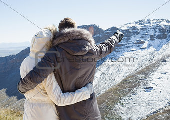 Loving couple in fur hood jackets looking at snowed mountain range