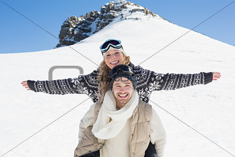 Wan piggybacking cheerful woman against snow covered hill