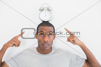 Close up of a man pointing at alarm clock over his head
