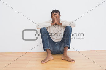 Afro man against wall with hands covering face