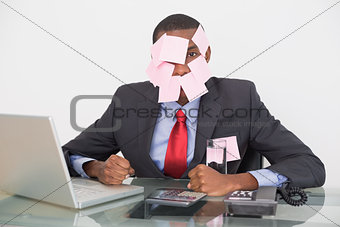 Afro businessman with blank notes on face and laptop