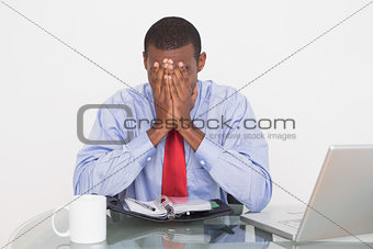 Businessman with hands covering face at desk