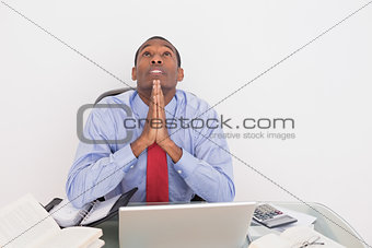 Afro businessman looking up with joined hands at desk