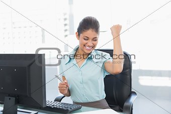 Happy businesswoman clenching fist at office desk