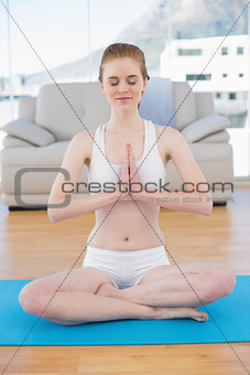 Toned woman in Namaste position with eyes closed at fitness studio