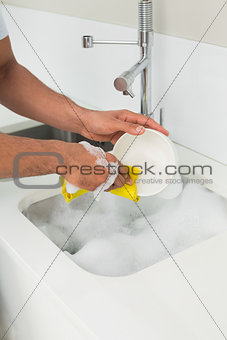 Hands doing the dishes at kitchen sink