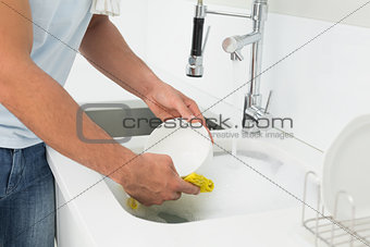 Mid section of man doing the dishes at kitchen sink