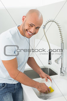 Smiling young man doing the dishes at kitchen sink