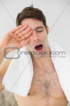 Shirtless man yawning as he rubs his eye