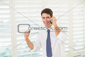 Smiling businessman using mobile phone while clenching fist