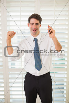 Cheerful businessman with mobile phone clenching fist in office