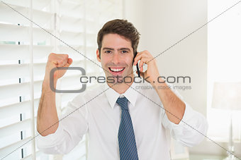 Smiling businessman using mobile phone while clenching fist
