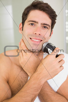 Smiling shirtless man shaving with electric razor
