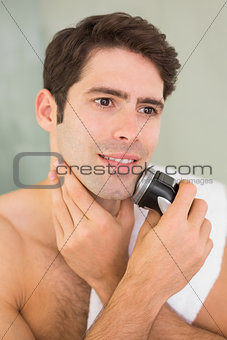 Handsome shirtless man shaving with electric razor