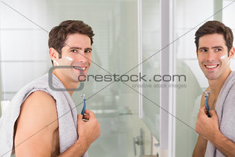 Smiling handsome man with reflection shaving in bathroom